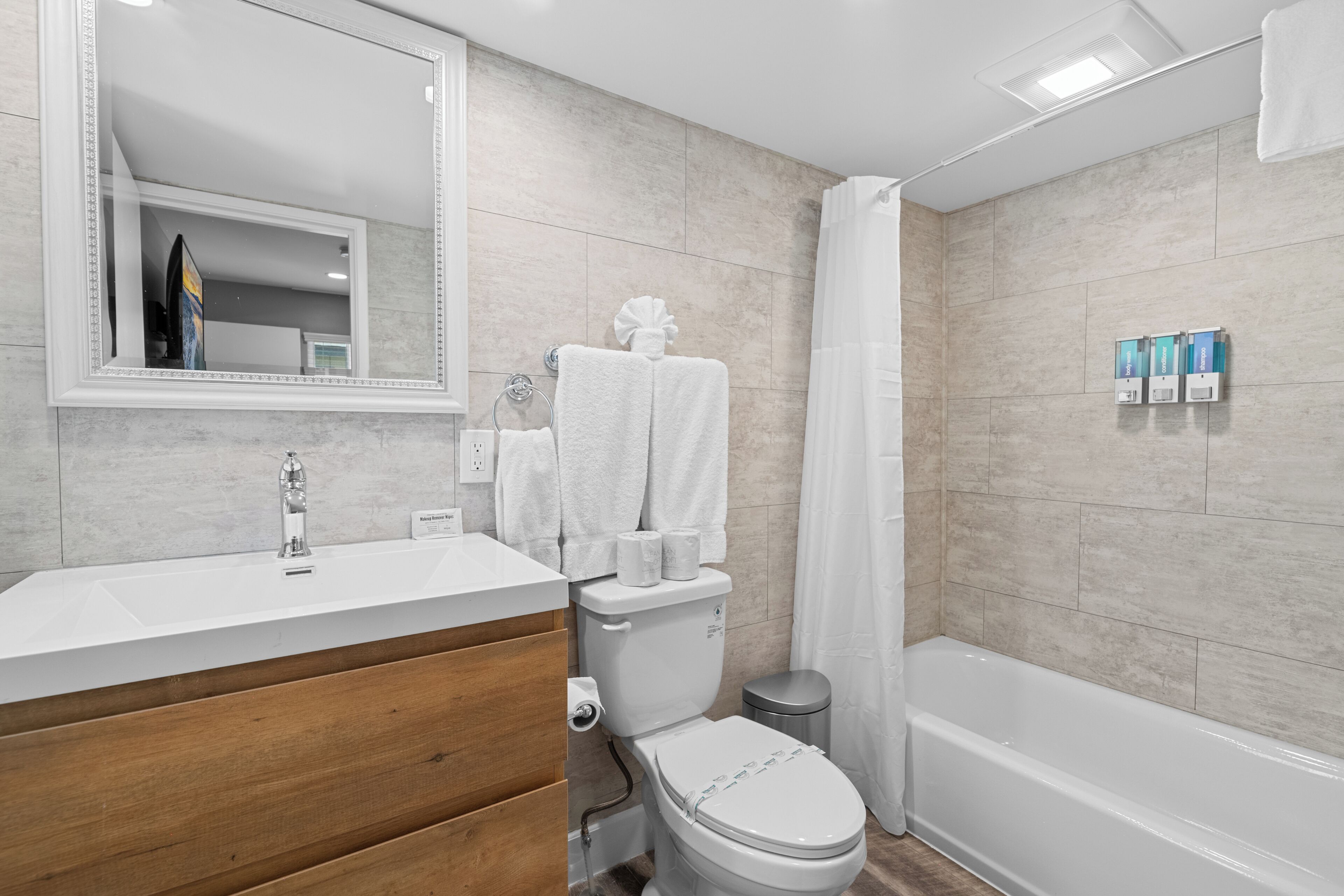 A modern bathroom with a white sink, wooden vanity, toilet, and bathtub.