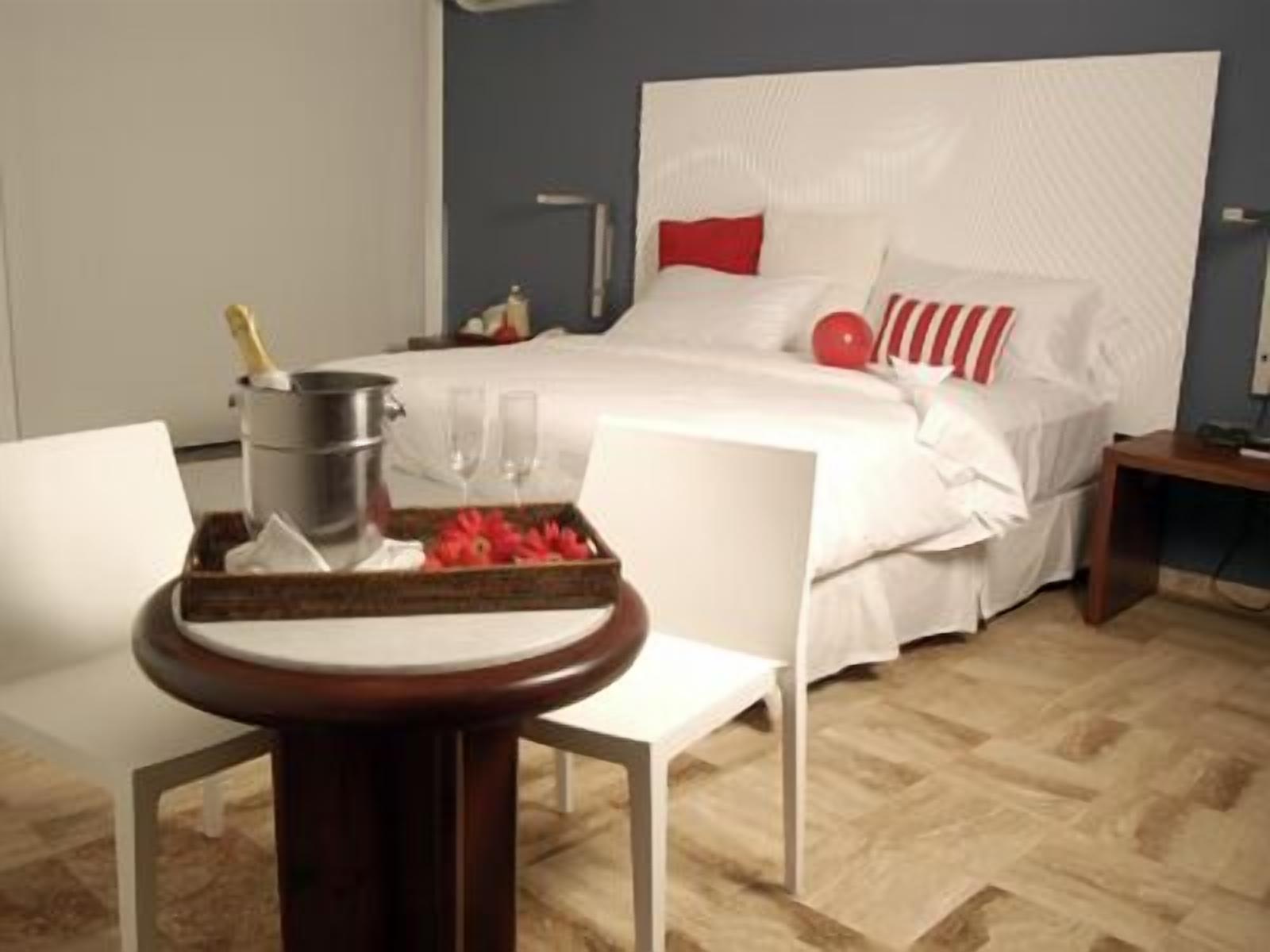 A hotel room with a bed, a bedside table, a chair, and a tray with a bottle and glasses.
