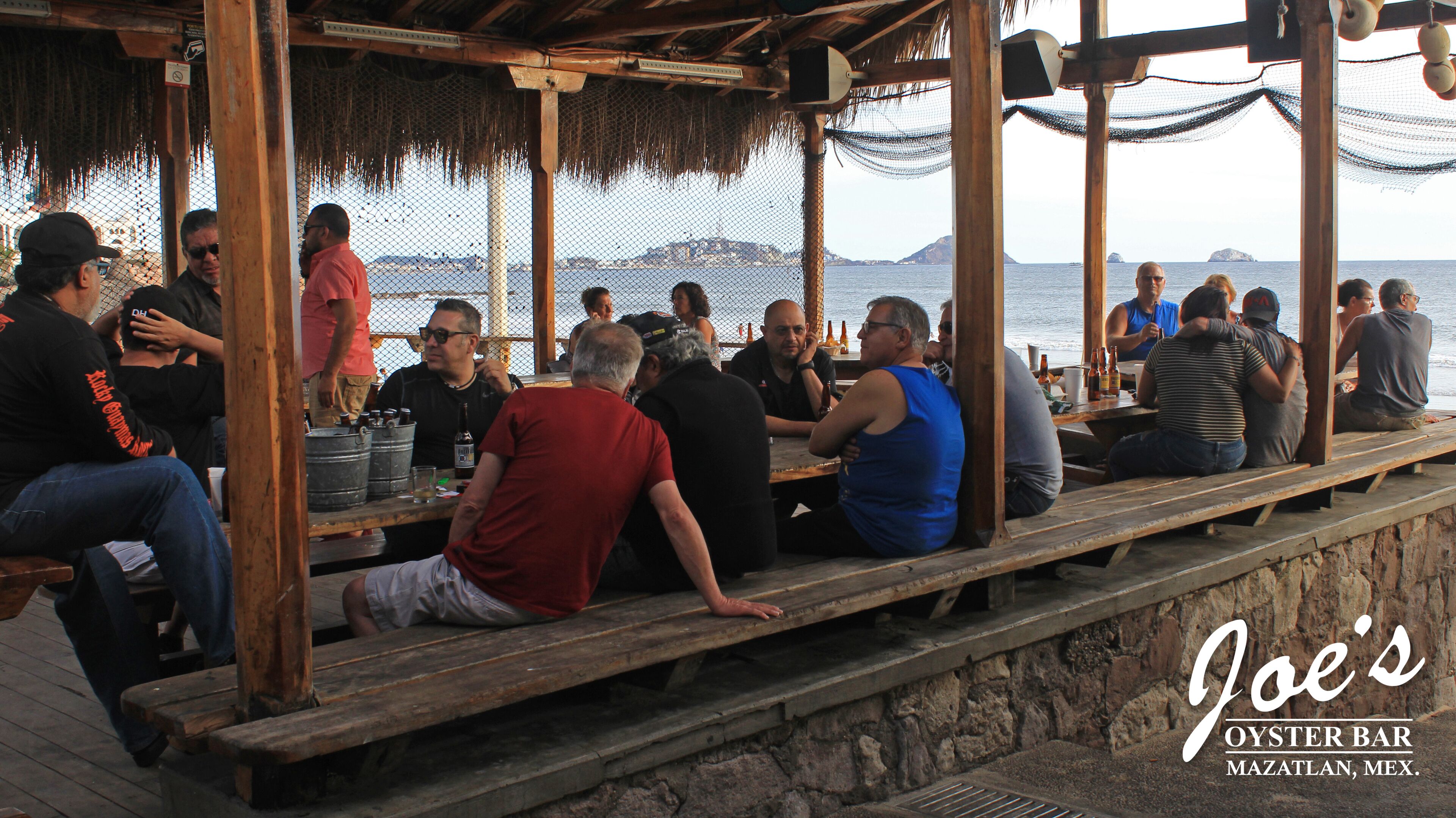 A wooden deck with people seated at tables, overlooking the sea.