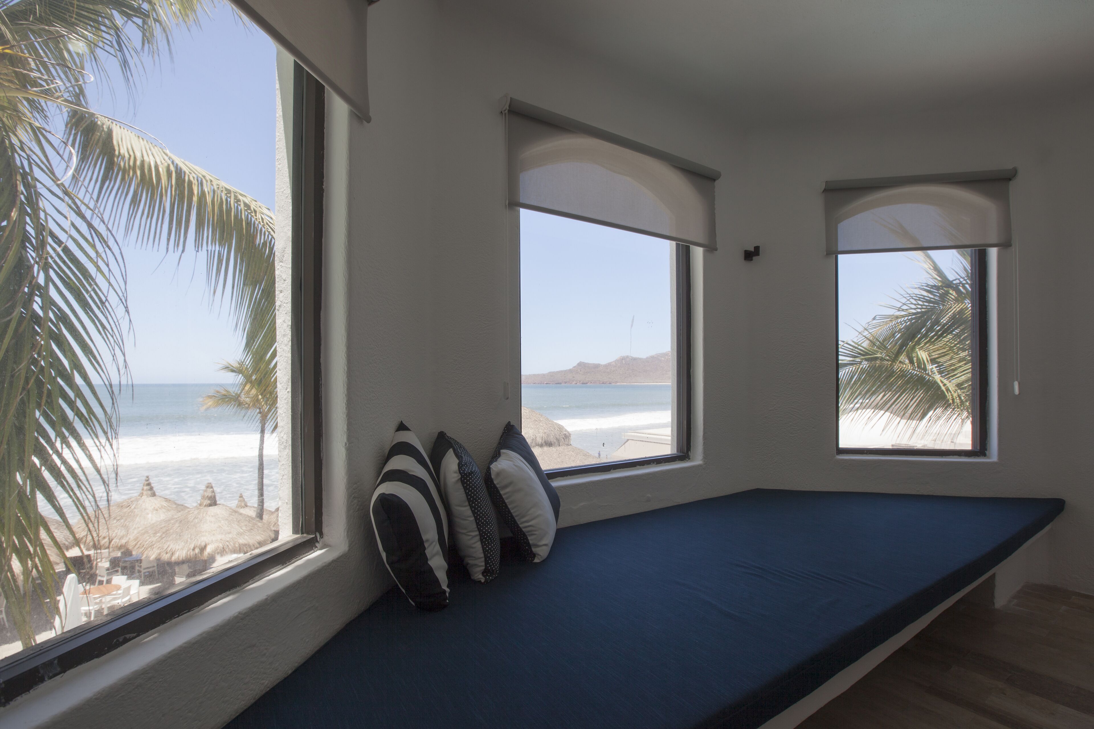 A room with a bed, three windows, and a view of the beach.