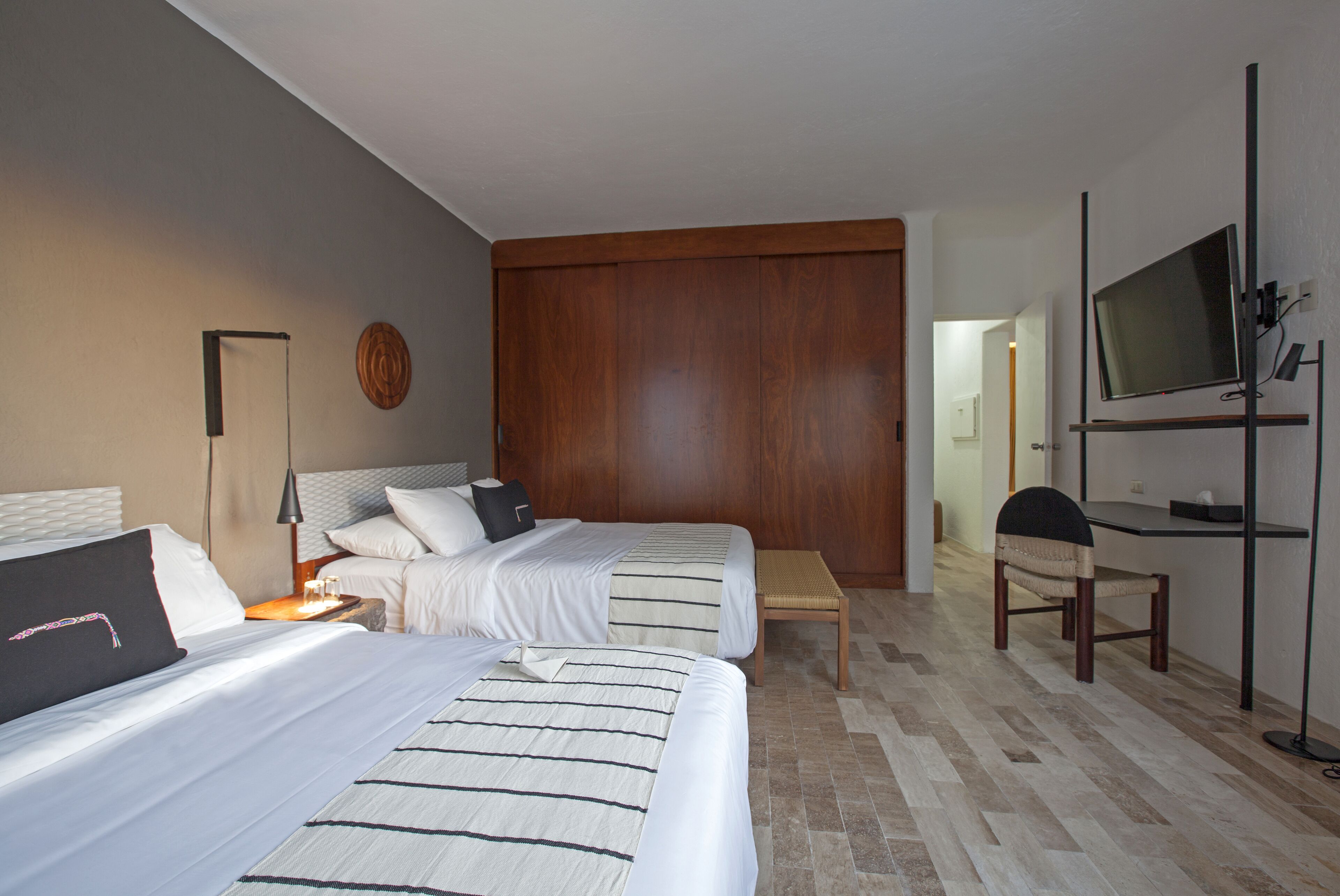 A hotel room with two beds, a wooden wardrobe, a television, and a bench.