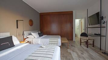 A hotel room with two beds, a wooden wardrobe, a television, and a bench.
