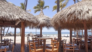 A beachside restaurant with thatched umbrellas and wooden tables and chairs, overlooking the ocean. - Gaviana Resort (Mazatlán)