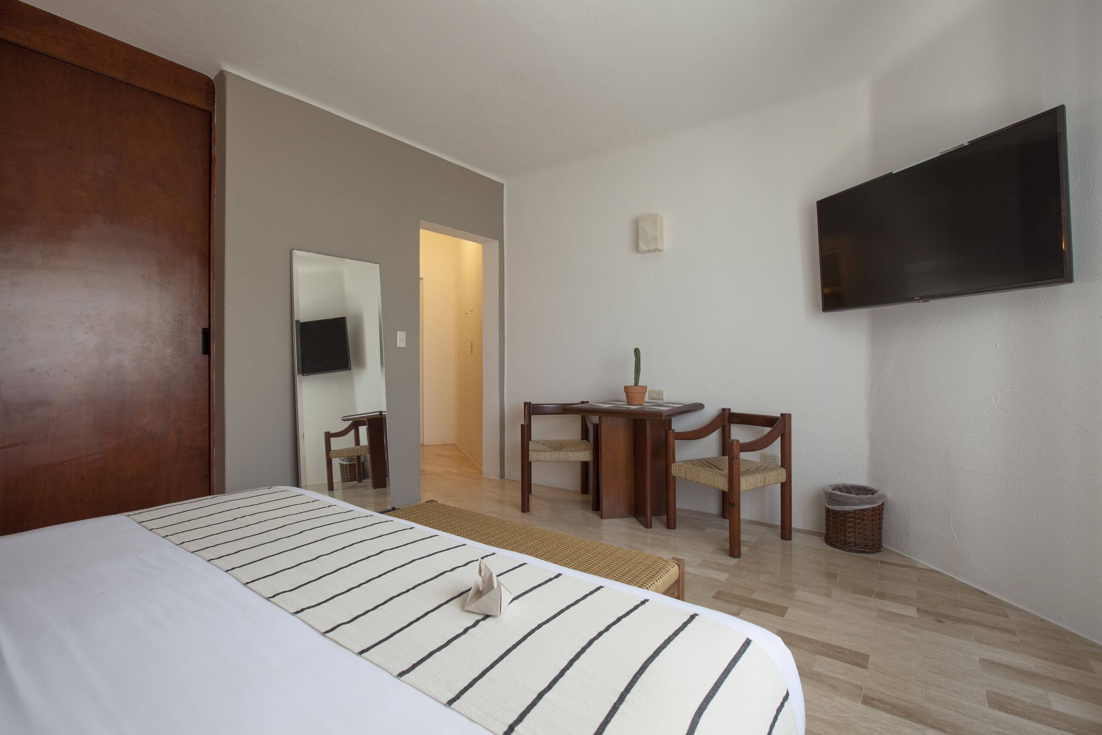 A hotel room with a bed, a desk with chairs, a television, and a small table with a potted plant.