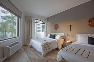 Habitación de hotel con dos camas, un ventanal con cortinas, una lámpara de pared y un radiador.