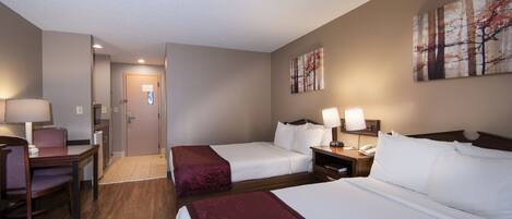 Quarto de hotel com duas camas, uma mesa e uma cadeira. Há uma porta que dá para o banheiro e um corredor.