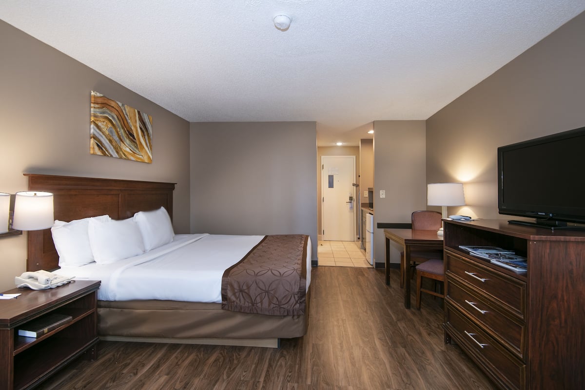A hotel room with a bed, bedside tables, a desk with a chair, a television, and a wall-mounted artwork.