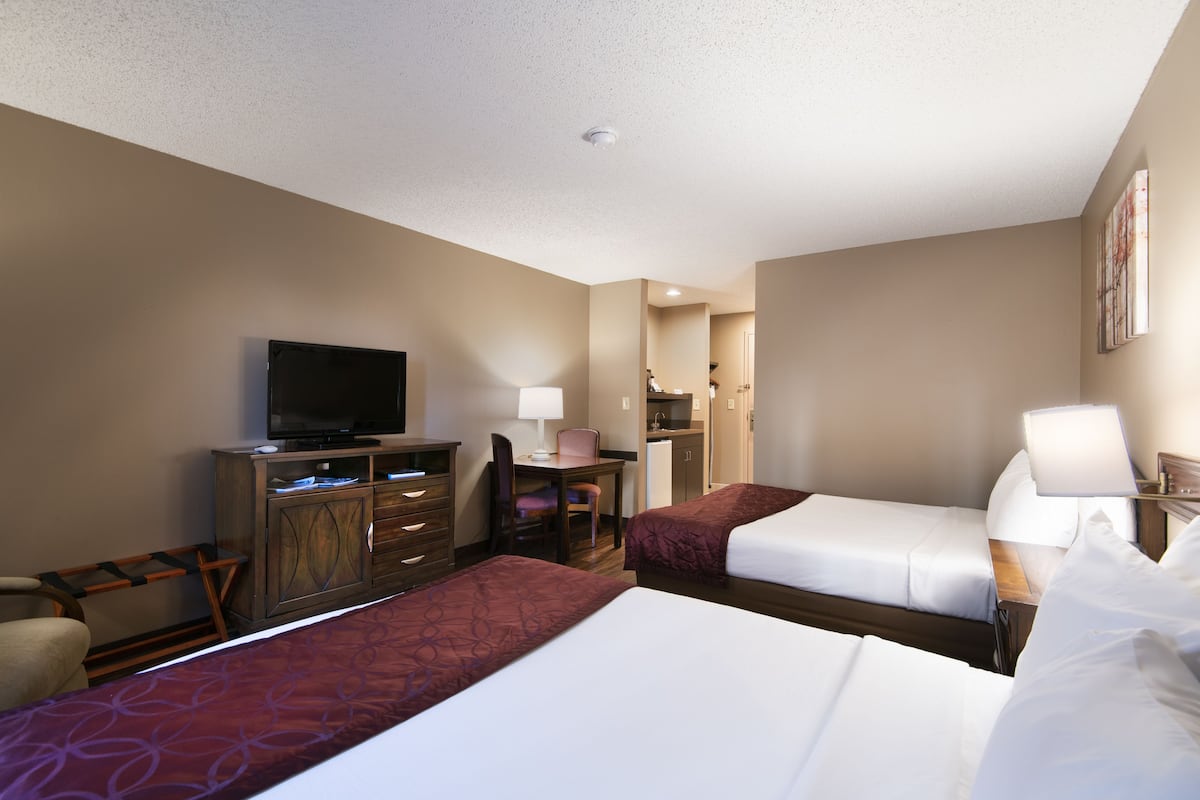 A hotel room with two beds, a television, a desk with a lamp, and a chair.