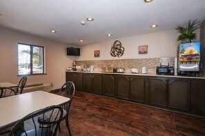 A kitchen with a dining table, chairs, a microwave, a coffee maker, and a juice dispenser.