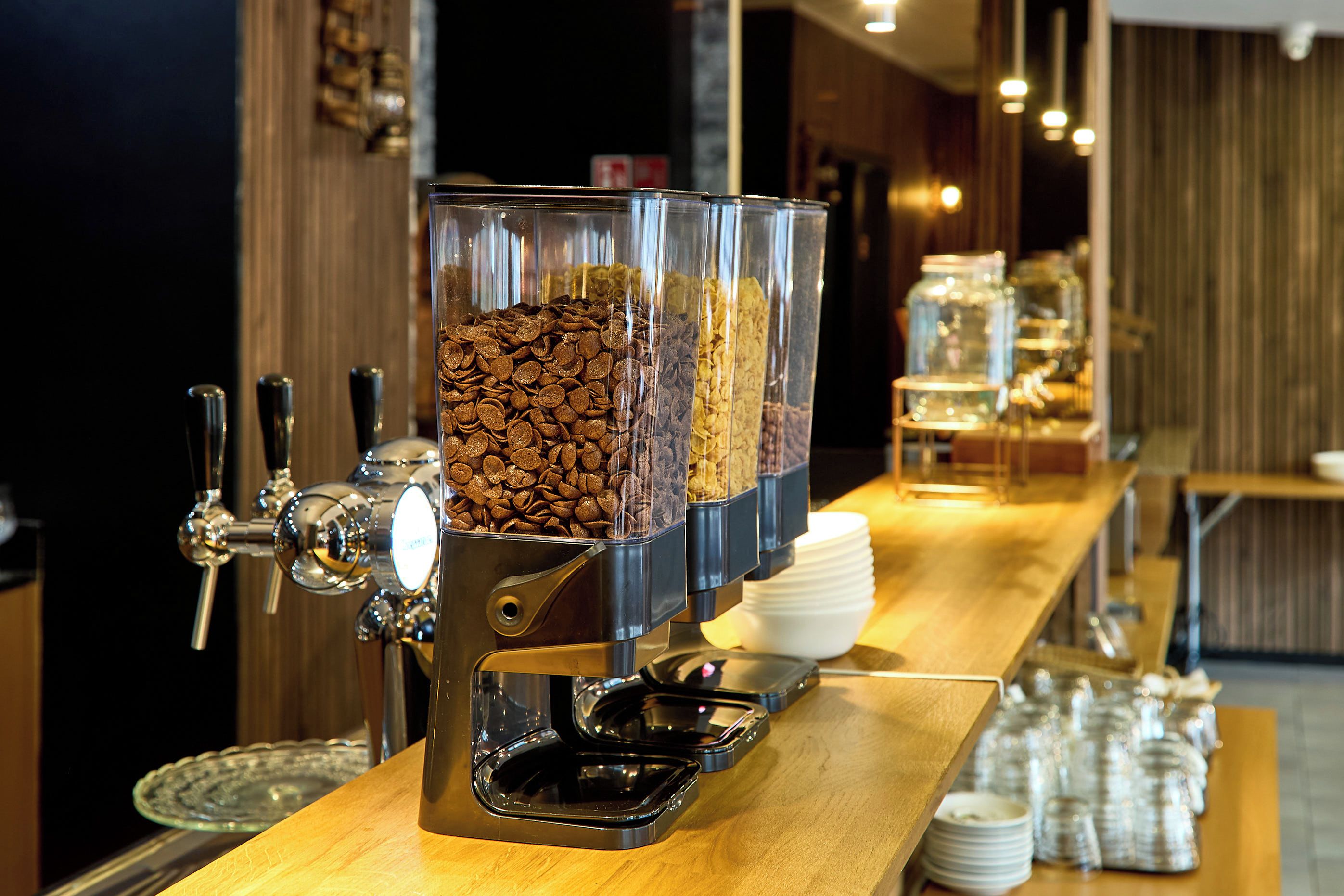 Un espace dédié au café, équipé de plusieurs distributeurs et d’une pile d’assiettes blanches.