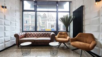 Un salón moderno con un sofá de cuero, dos sillones y una mesita. Grandes ventanales ofrecen vistas a la ciudad.