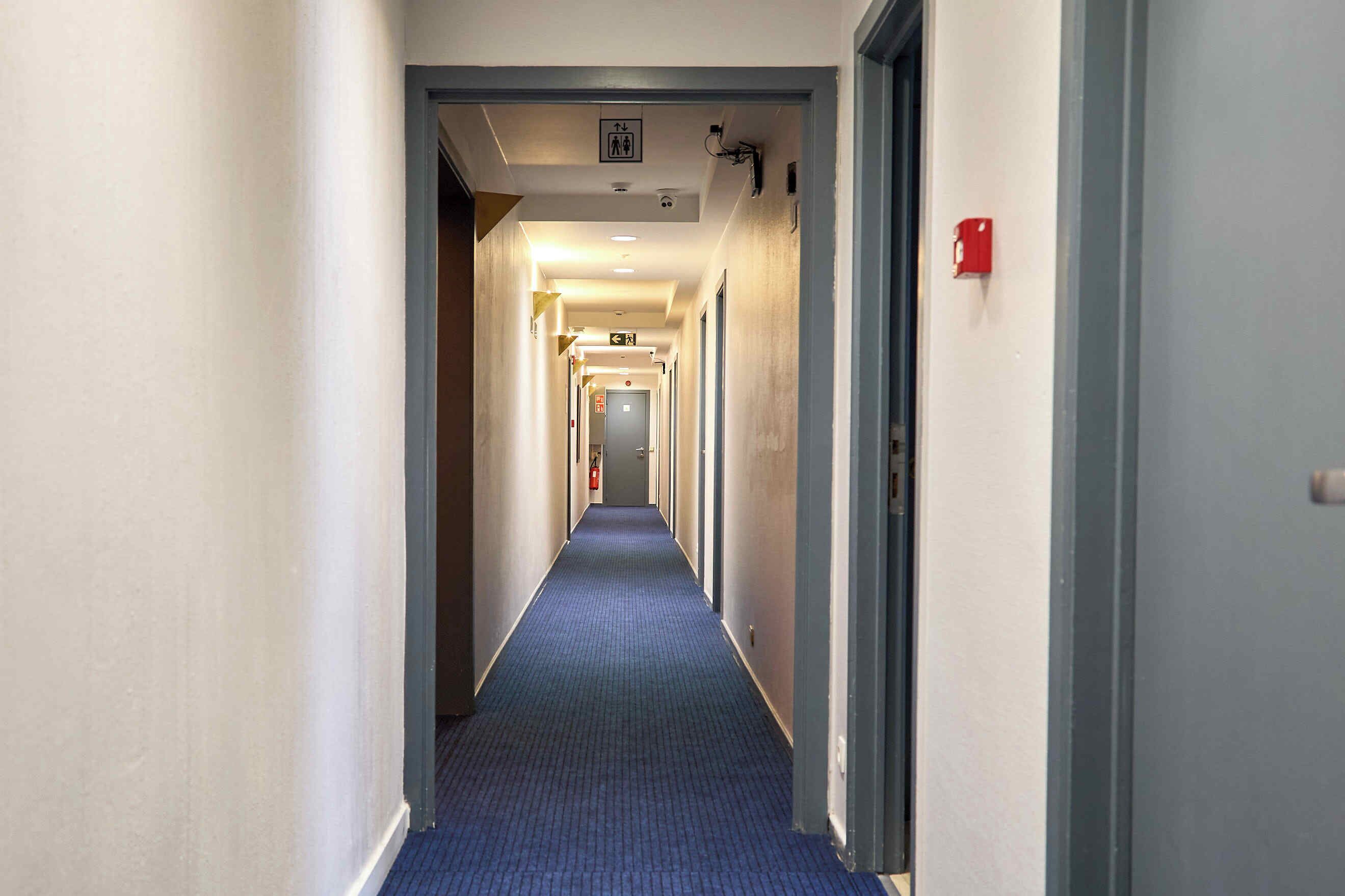 Un largo y estrecho pasillo de hotel con alfombra azul, paredes blancas y puertas a ambos lados.