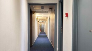 A long, narrow hotel corridor with a blue carpet, white walls, and doors on both sides. - Hotel Europacity (Brussels)