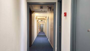 Un largo y estrecho pasillo de hotel con alfombra azul, paredes blancas y puertas a ambos lados.