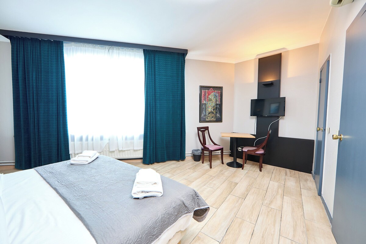 A hotel room with two beds, a desk, a chair, a TV, and a painting on the wall.