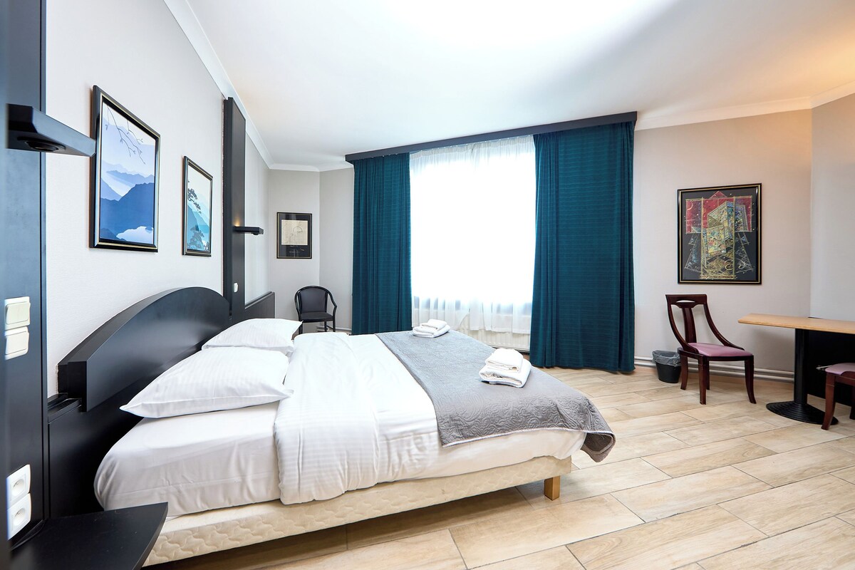 A hotel room with a bed, a desk, a chair, and artwork on the walls.