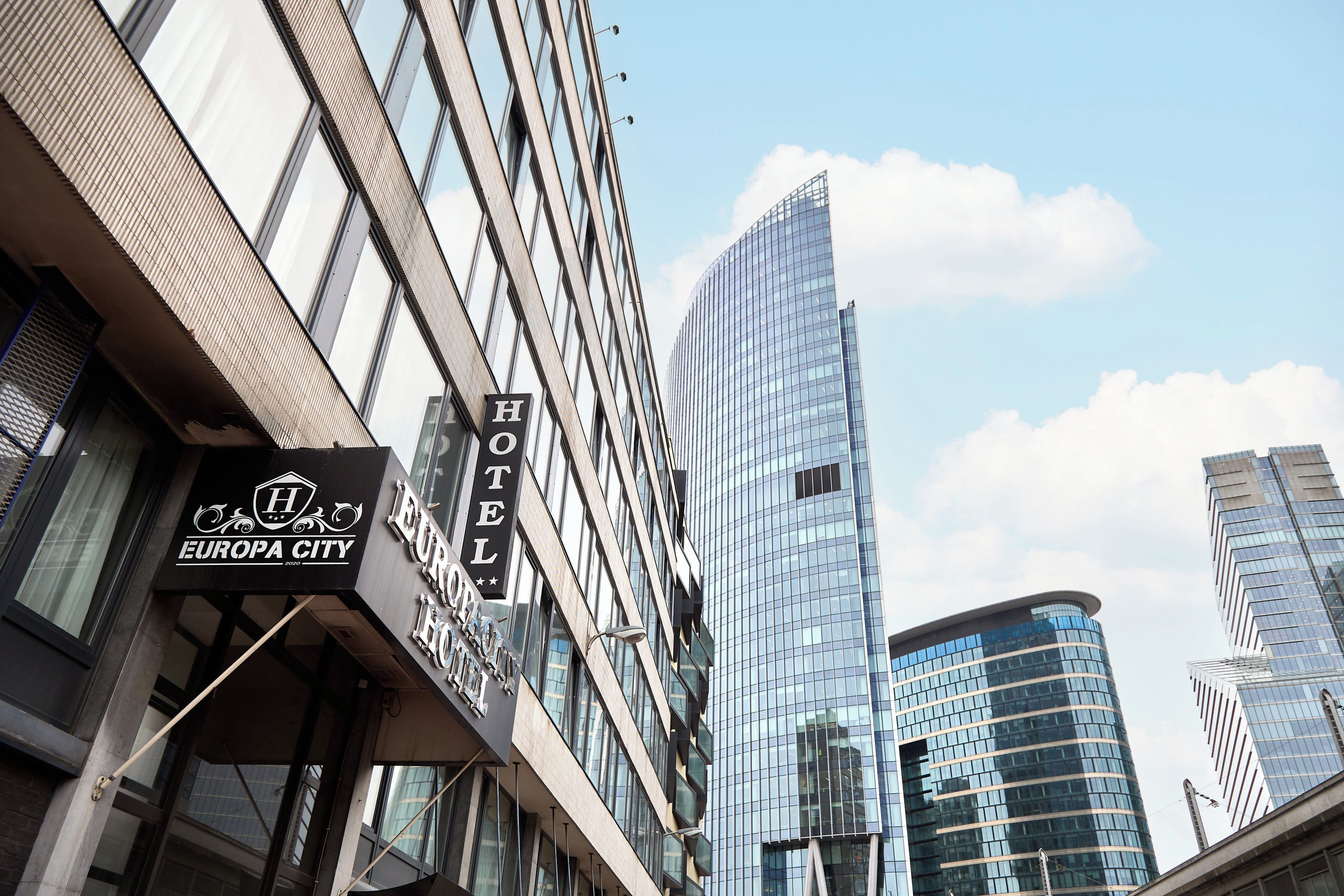 Un hôtel avec une enseigne indiquant « EUROPA CITY HOTEL » et un bâtiment moderne en verre en arrière-plan.