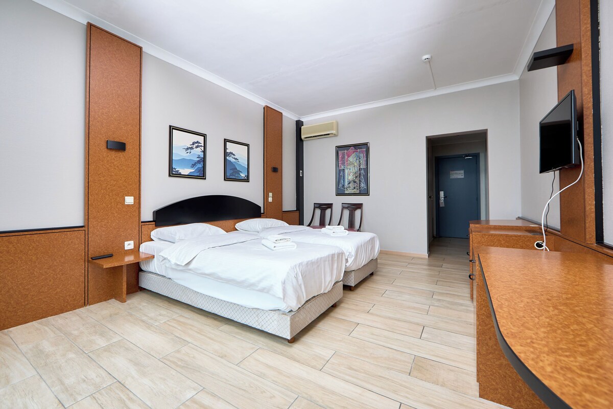 Ein Hotelzimmer mit zwei Betten, einem Holztisch, einem Flachbildfernseher und Bildern an den Wänden.
