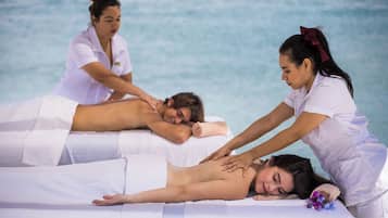 A massage therapy session with a client lying on a massage table, a therapist attending to the client, and another person observing.