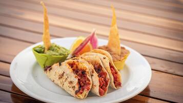 A plate with three tacos, a bowl of guacamole, and a slice of lime on a wooden table.