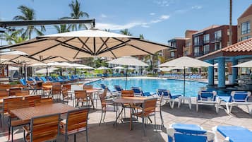 A poolside area with lounge chairs, umbrellas, and wooden tables.