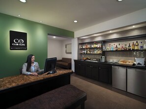 Una recepción con un ordenador, una zona de bar con diferentes botellas y una cocina con electrodomésticos.