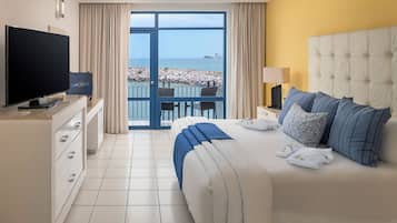 A hotel room with a bed, a TV, a balcony with a view of the sea, and a chair.