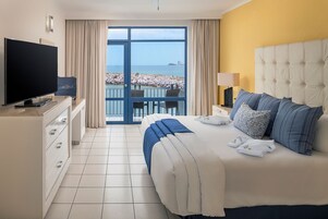 Habitación de hotel con cama, televisión, balcón y vista al mar, además de una silla.