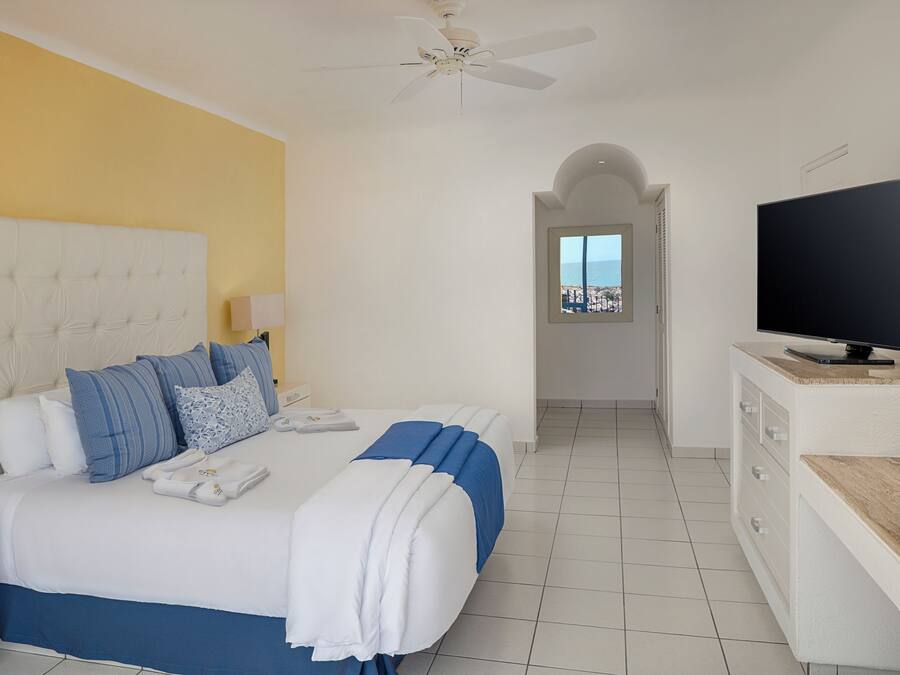 A hotel room with a bed, a television, and a view of the sea through a window.