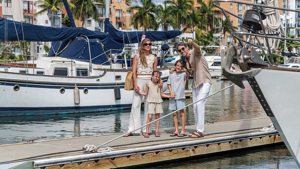 Un grupo de personas en un muelle, con barcos y edificios al fondo.