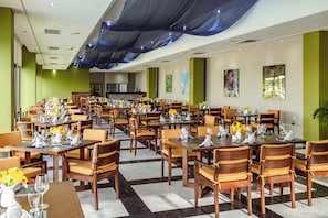 A spacious dining area with multiple tables and chairs, a bar in the background, and artwork on the walls. - El Cid El Moro Beach Hotel (Mazatlán)