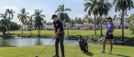 A golf course with a pond, palm trees, and a clubhouse in the background.