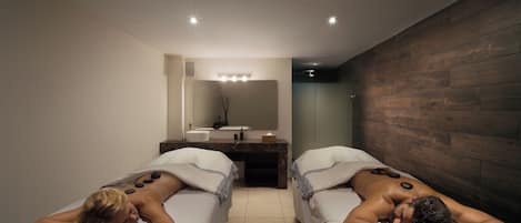Dos camillas de masoterapia en una habitación moderna con pared de madera, un espejo y un lavamanos.