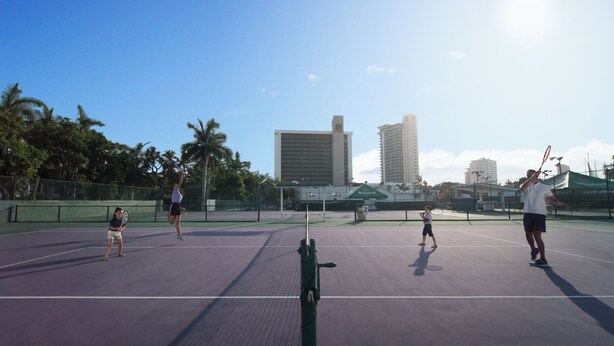 An outdoor tennis court with a net, surrounded by a fence, and buildings in the background. - El Cid El Moro Beach Hotel (Mazatlán)