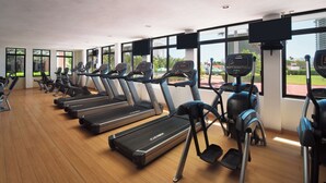 A gym with treadmills and ellipticals, large windows, and a view of greenery and buildings. - El Cid El Moro Beach Hotel (Mazatlán)