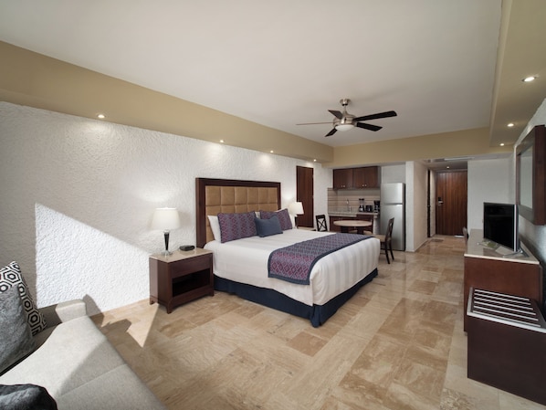 A hotel room with a bed, bedside table, lamp, and a kitchenette area.