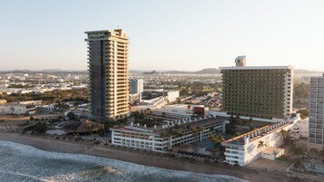 Un paisaje urbano costero con rascacielos, una playa y un hotel con varios pisos y balcones.