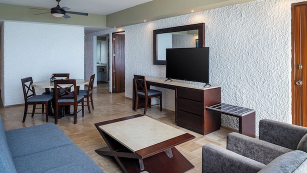 A modern living room with a flat-screen TV, a dining area with wooden chairs, and a sofa. - El Cid El Moro Beach Hotel (Mazatlán)