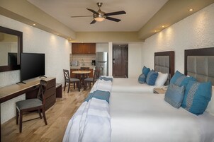 Habitación de hotel con cama, escritorio, televisor, ventilador de techo y kitchenette.
