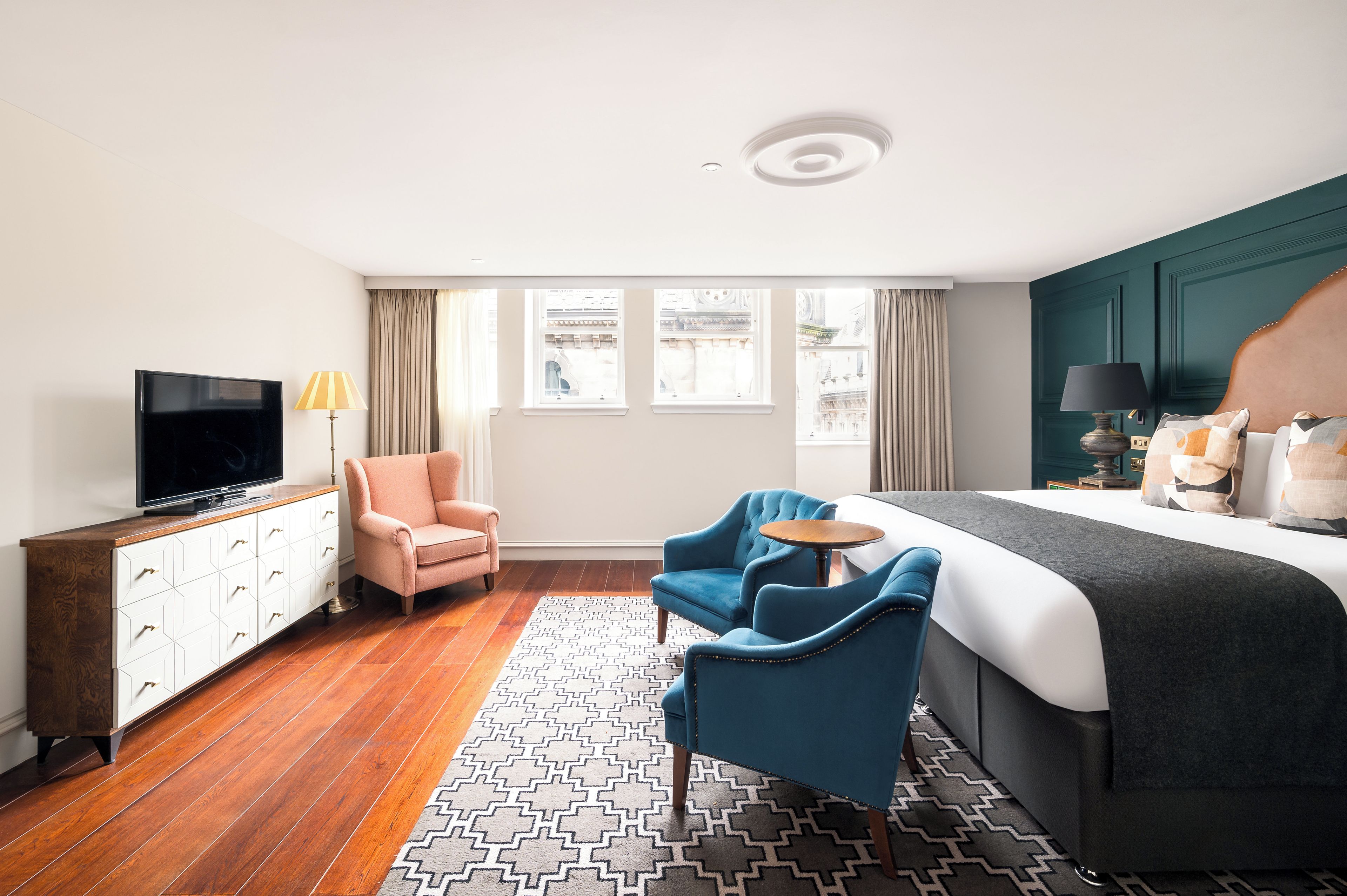 A hotel room with a bed, a TV, a desk, a chair, and a window with a view of buildings.