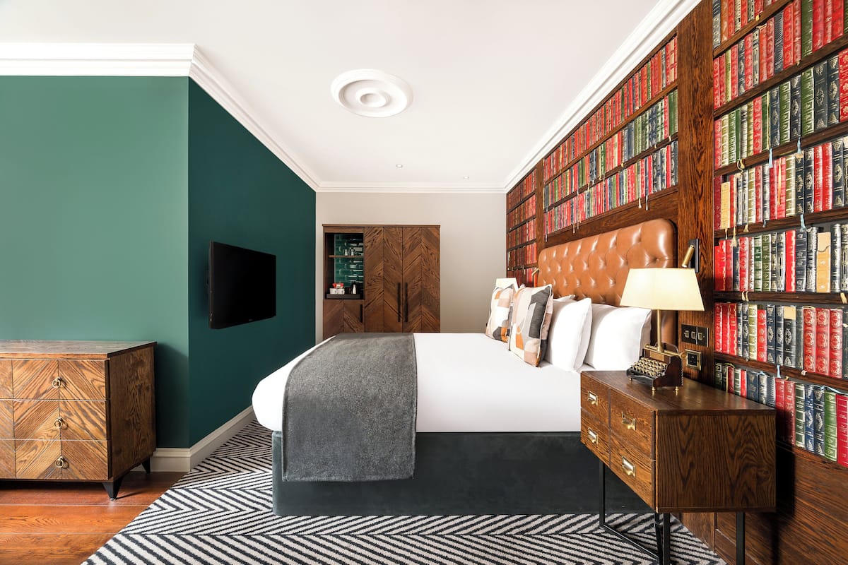 A bedroom with a large bed, a bookshelf, a dresser, and a television.
