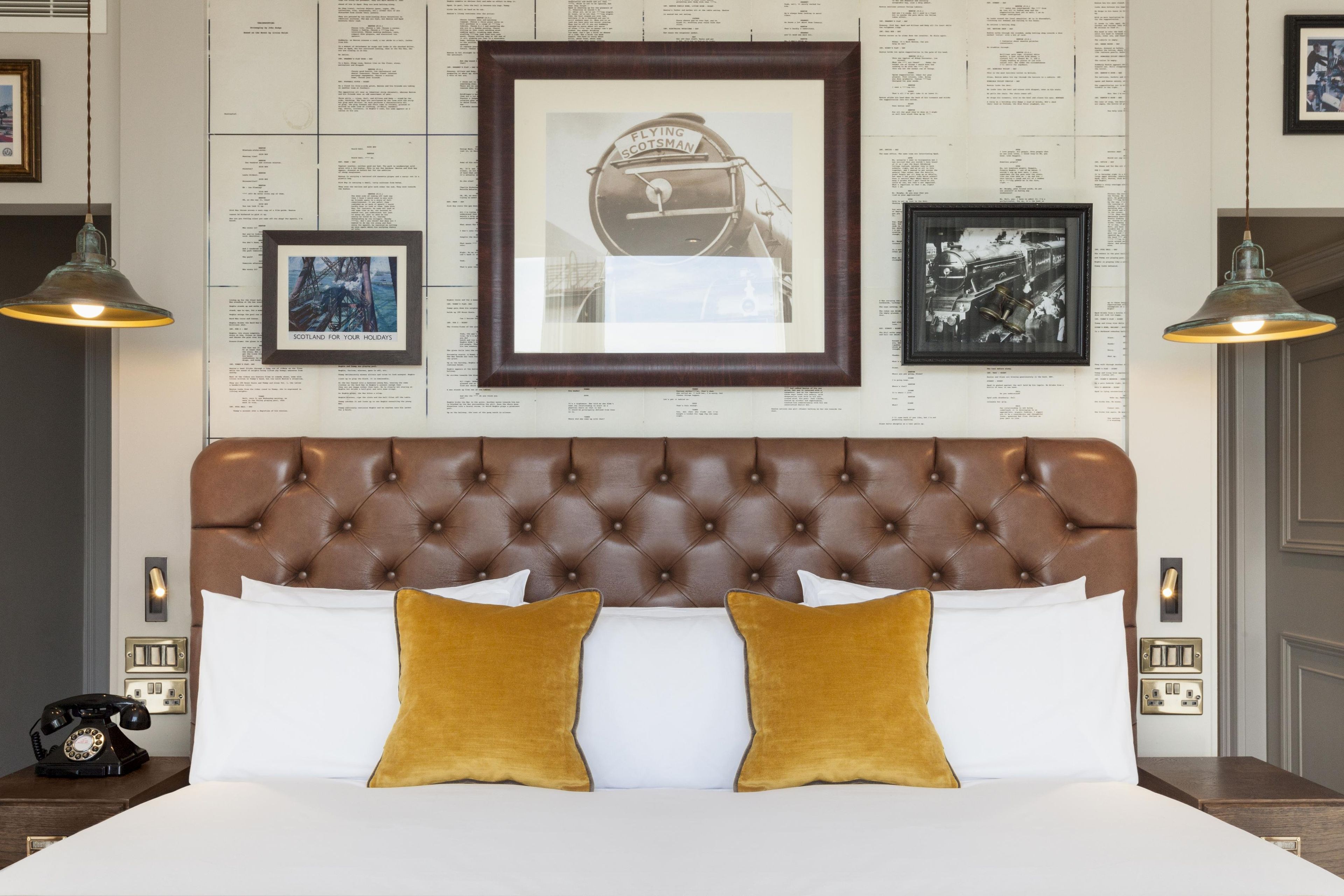 A bedroom with a tufted headboard, a bed with white linens, two mustard-colored pillows, and framed pictures on the wall.