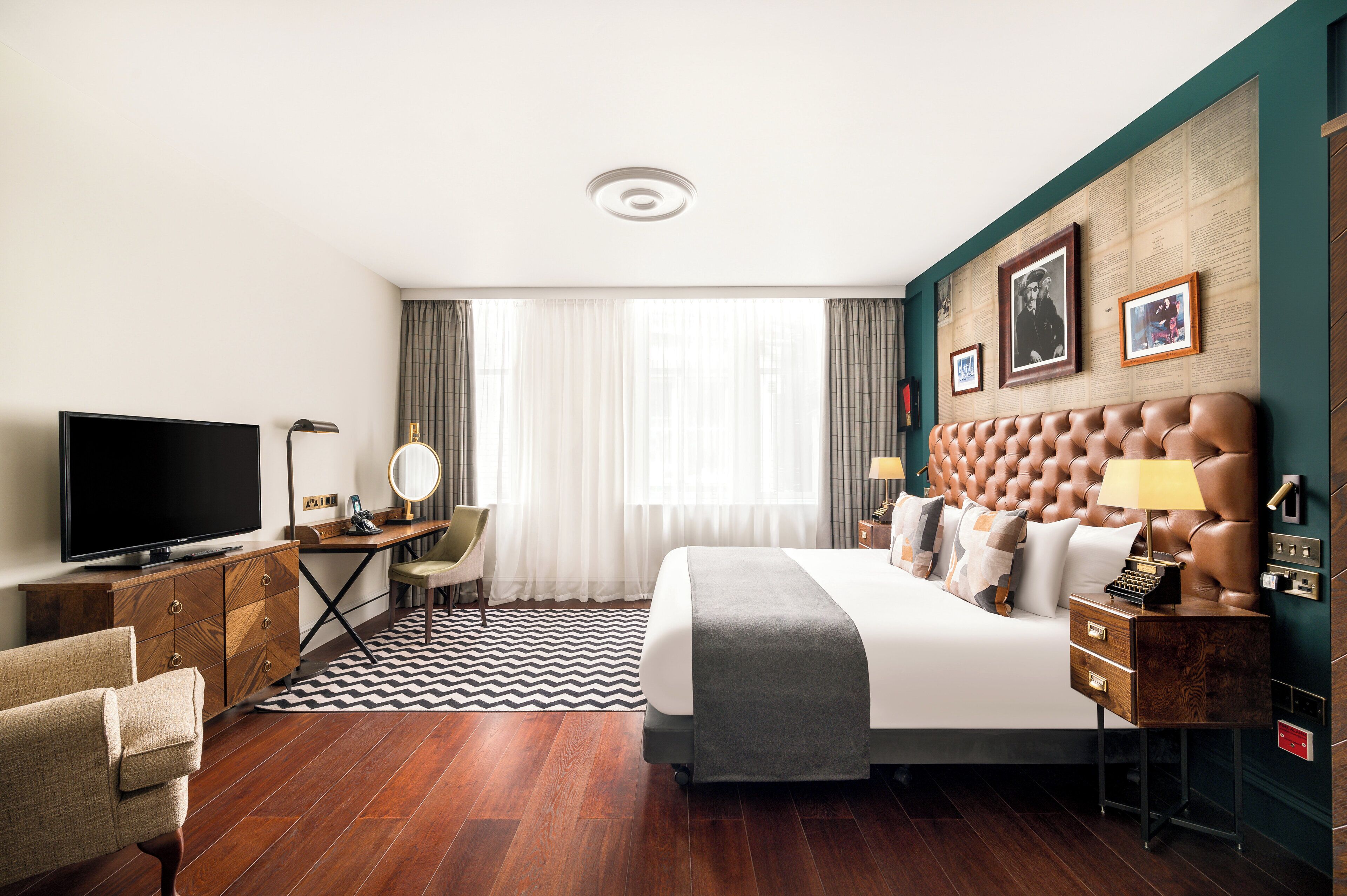 A hotel room with a large bed, a desk with a computer, a television, and a seating area with a chair.