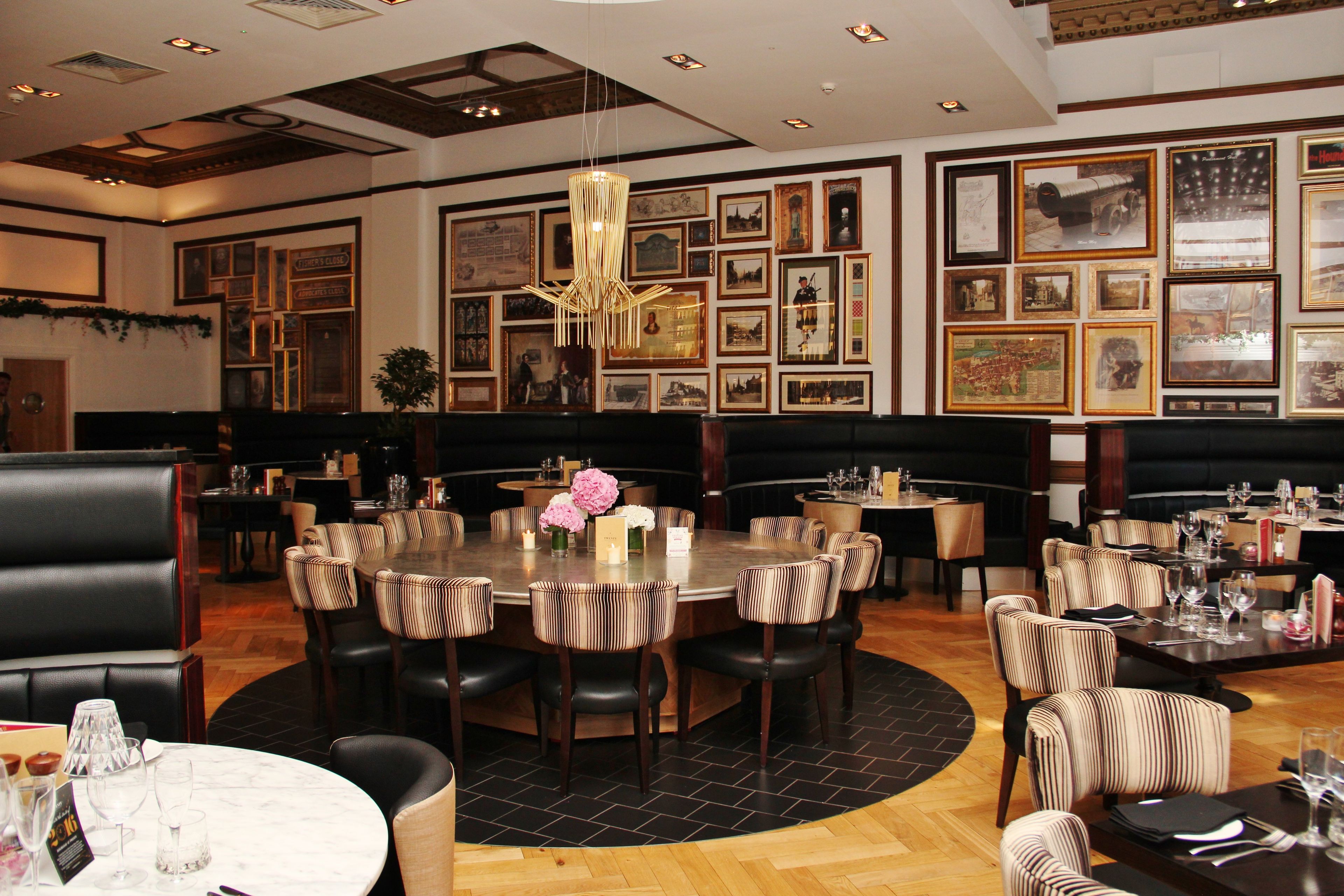 Un restaurant avec une grande table ronde au centre, entourée de chaises à rayures, des tableaux encadrés aux murs et un luminaire suspendu.