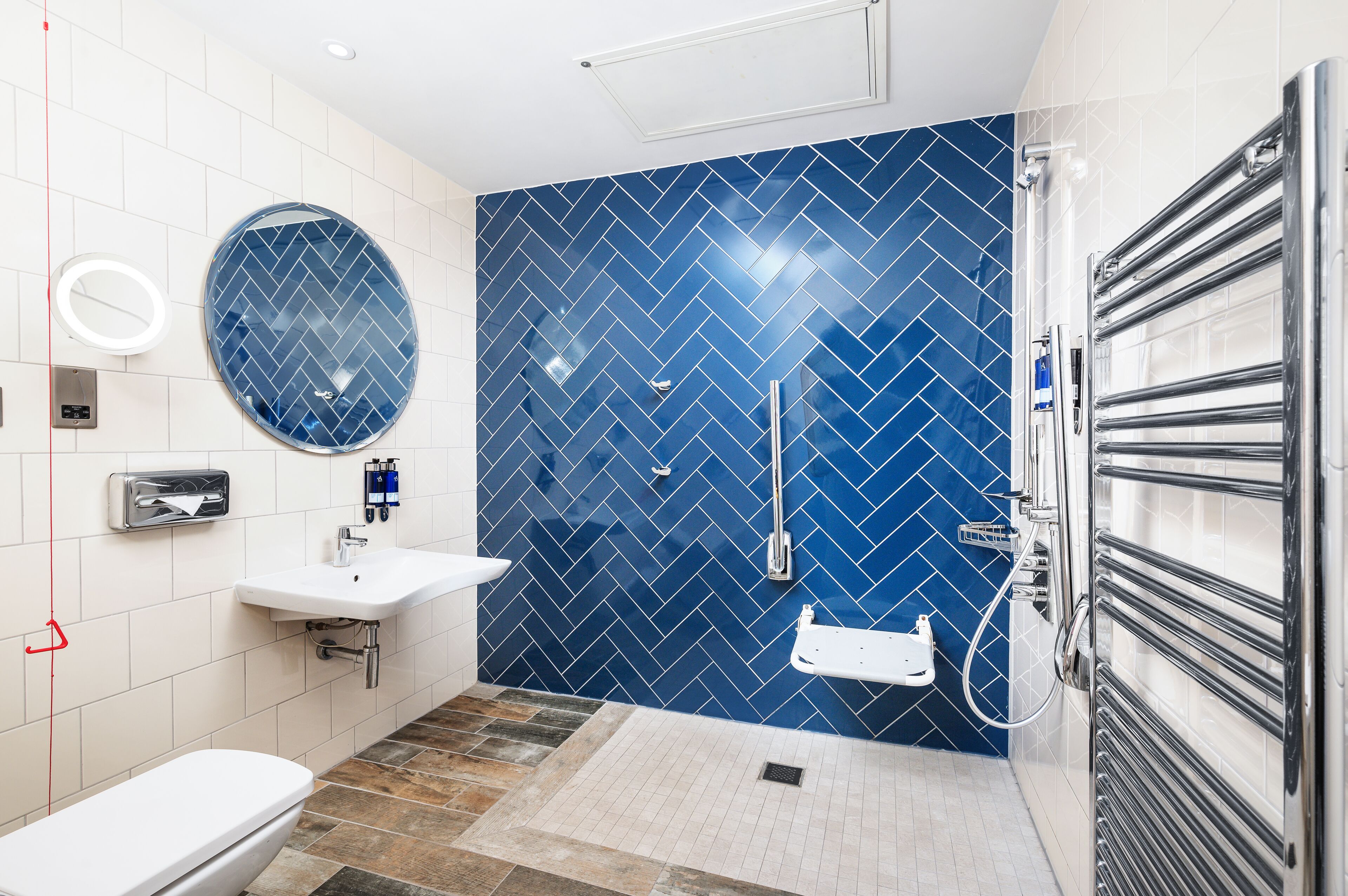 Un baño moderno con inodoro blanco, lavamanos, espejo y ducha con pared de azulejos azules.