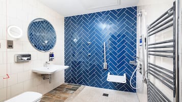 Un baño moderno con inodoro blanco, lavamanos, espejo y ducha con pared de azulejos azules.