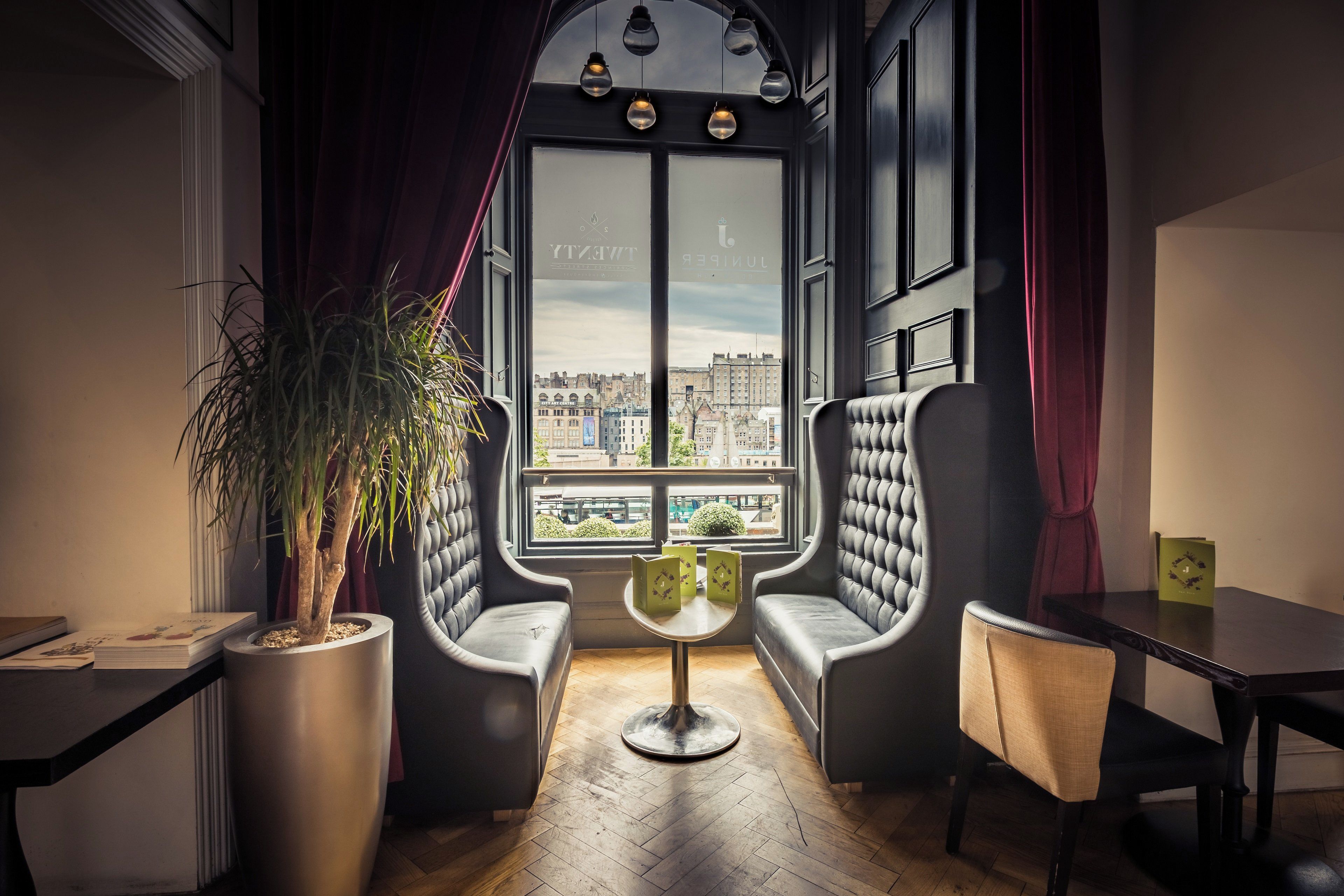 Een kamer met een groot raam, twee fauteuils, een bijzettafeltje en een potplant.
