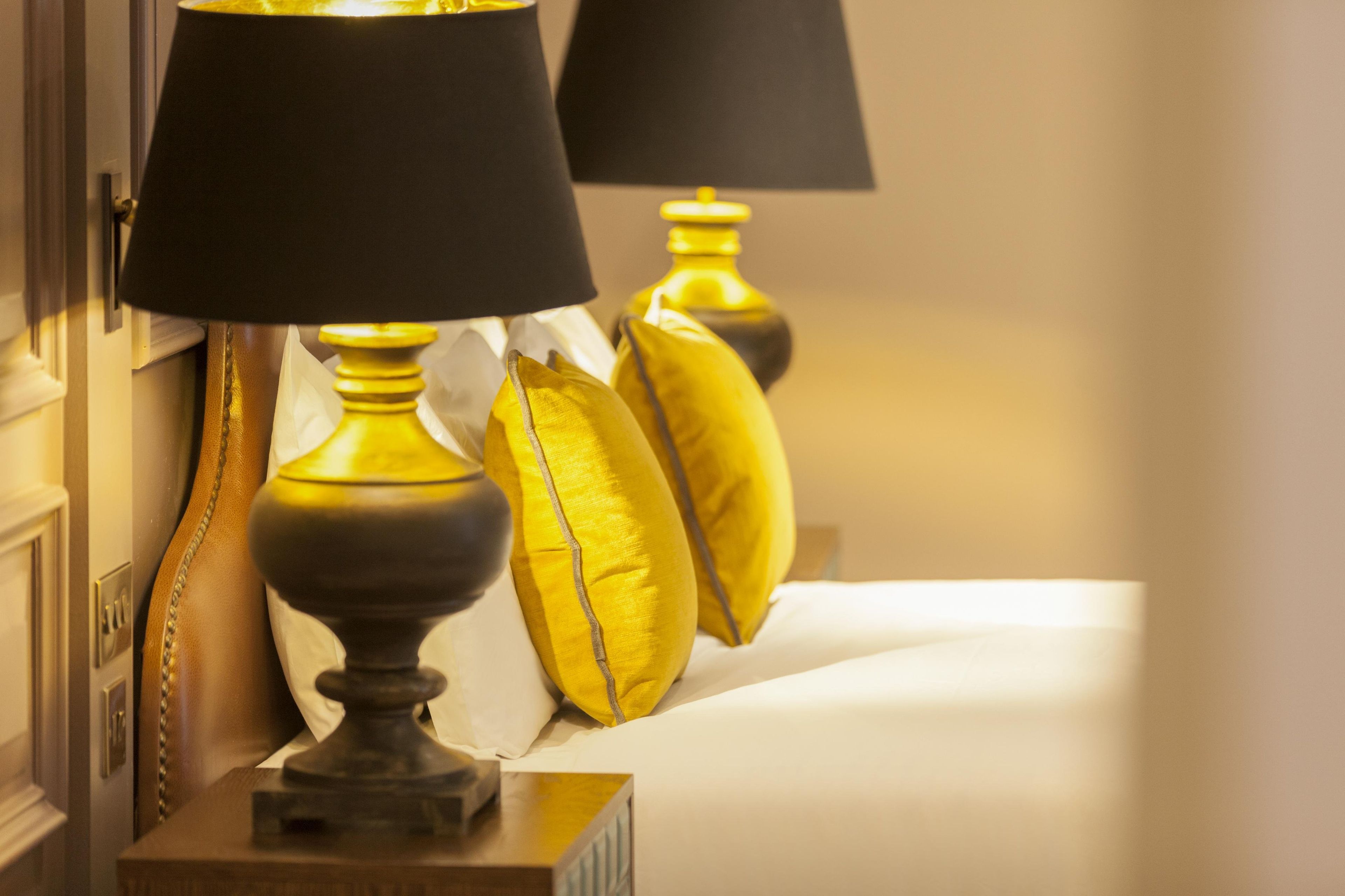 A close-up of a lamp with a black shade and a decorative base, placed on a surface with a white cloth.
