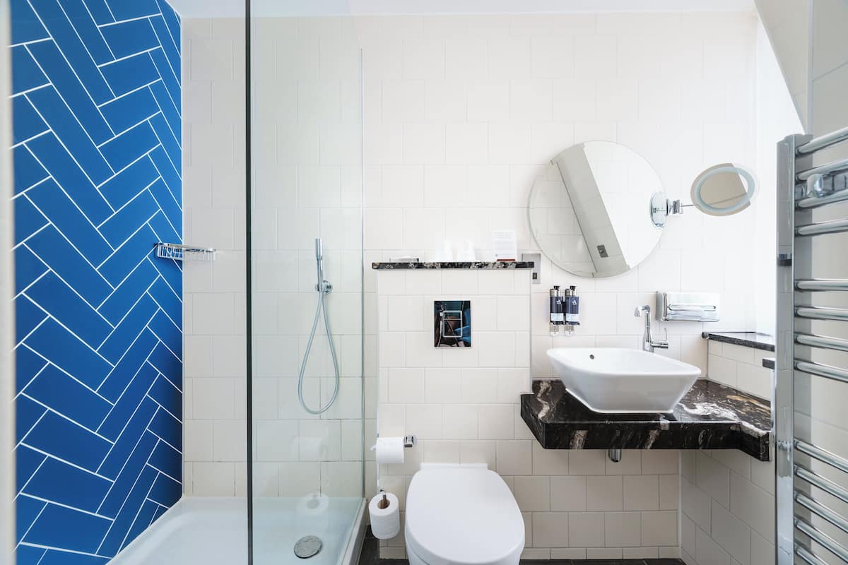 A modern bathroom with a glass-enclosed shower, a white toilet, a sink with a marble countertop, and a large mirror.
