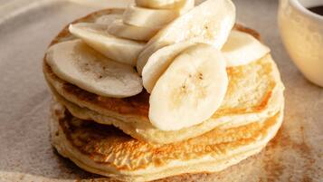 A stack of pancakes with banana slices on top, served on a plate with a dusting of cinnamon.